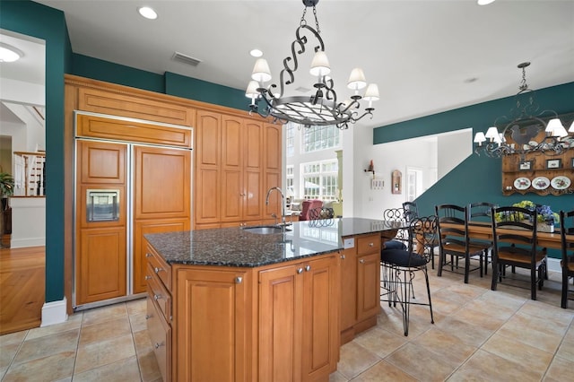 kitchen with a center island with sink, visible vents, paneled built in fridge, a sink, and a notable chandelier