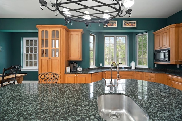 kitchen with dark stone counters, glass insert cabinets, black microwave, and a sink