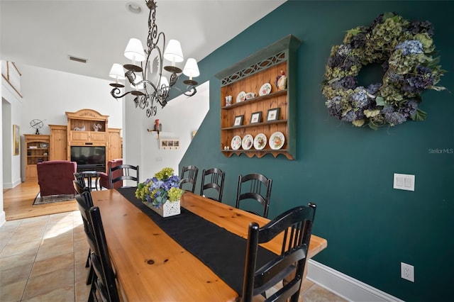 dining space featuring visible vents, a glass covered fireplace, light tile patterned floors, baseboards, and a chandelier