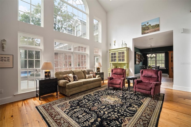 living room featuring baseboards, high vaulted ceiling, an inviting chandelier, and light wood-style flooring