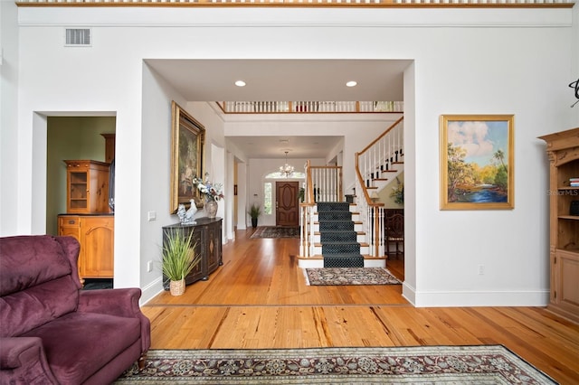 foyer entrance with an inviting chandelier, stairway, light wood-style floors, and visible vents