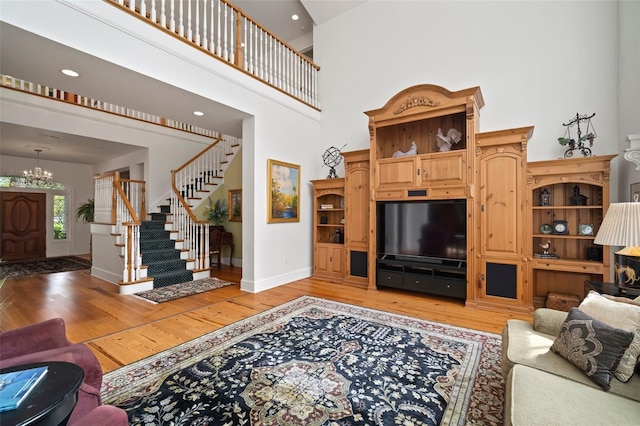 living area featuring stairway, a notable chandelier, a high ceiling, and light wood-style flooring