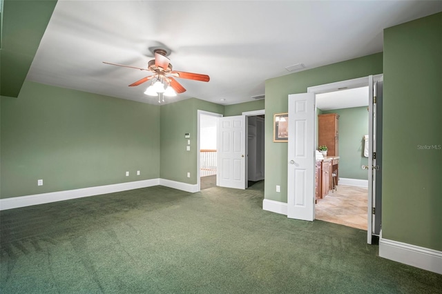 unfurnished bedroom with a walk in closet, baseboards, a ceiling fan, and dark carpet