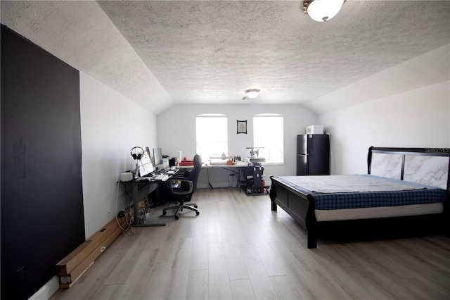 bedroom featuring light wood-type flooring, a textured ceiling, vaulted ceiling, and freestanding refrigerator