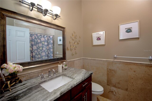 full bathroom with vanity, a shower with curtain, a wainscoted wall, tile walls, and toilet