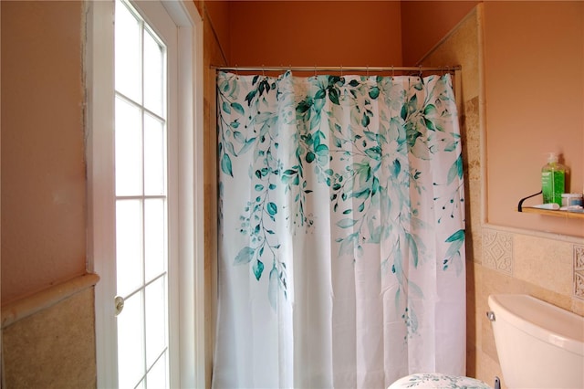 bathroom with a shower with curtain, tile walls, toilet, and a wainscoted wall