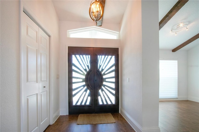 foyer featuring a wealth of natural light, a notable chandelier, beam ceiling, and wood finished floors