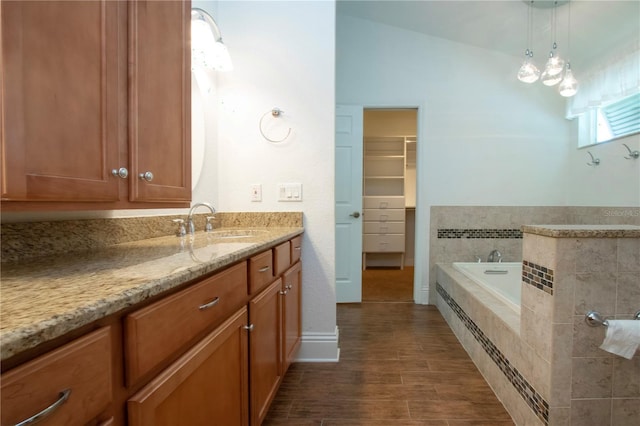 bathroom with tiled bath, vanity, a walk in closet, and wood finished floors