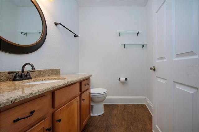 bathroom featuring toilet, vanity, baseboards, and wood finished floors