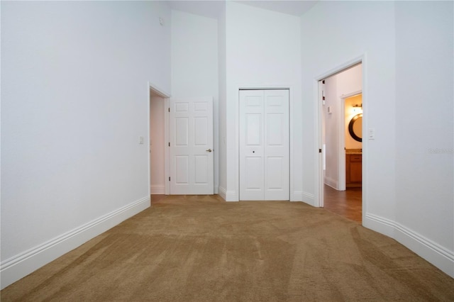 unfurnished bedroom featuring a high ceiling, carpet flooring, baseboards, and a closet