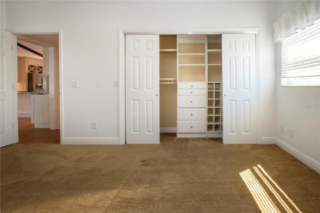 unfurnished bedroom featuring baseboards, stainless steel fridge, and carpet flooring