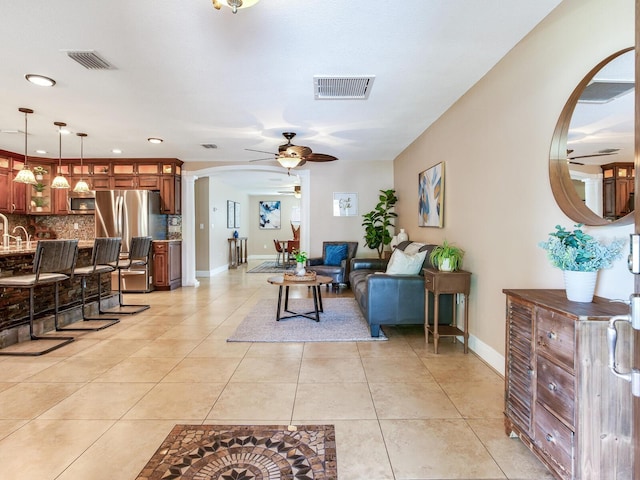 living room with light tile patterned floors, visible vents, arched walkways, and ceiling fan