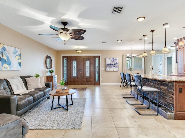 living room with ceiling fan with notable chandelier, light tile patterned floors, baseboards, and visible vents