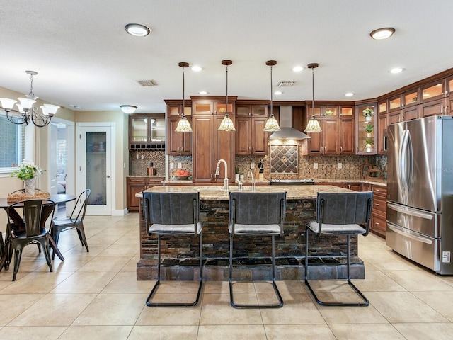 kitchen with wall chimney exhaust hood, brown cabinetry, visible vents, and freestanding refrigerator