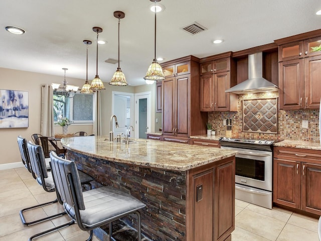 kitchen featuring visible vents, wall chimney range hood, light stone countertops, an island with sink, and stainless steel electric range