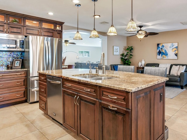 kitchen with light tile patterned floors, a kitchen island with sink, a sink, stainless steel appliances, and backsplash