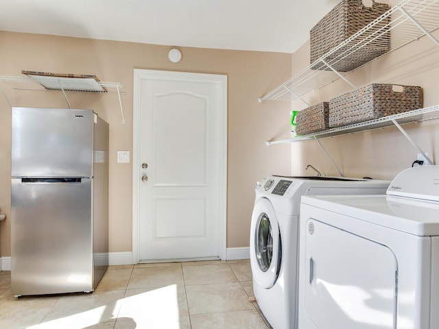 clothes washing area with washer and dryer, laundry area, light tile patterned floors, and baseboards