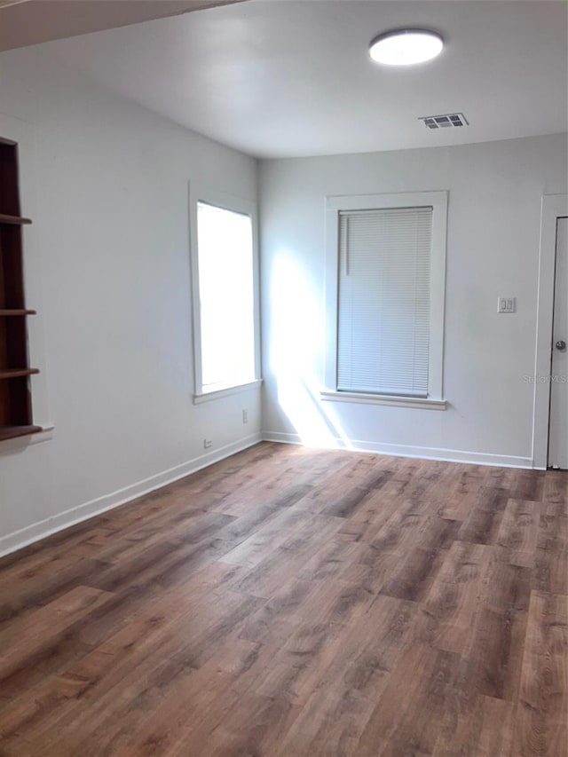 empty room featuring baseboards, wood finished floors, and visible vents
