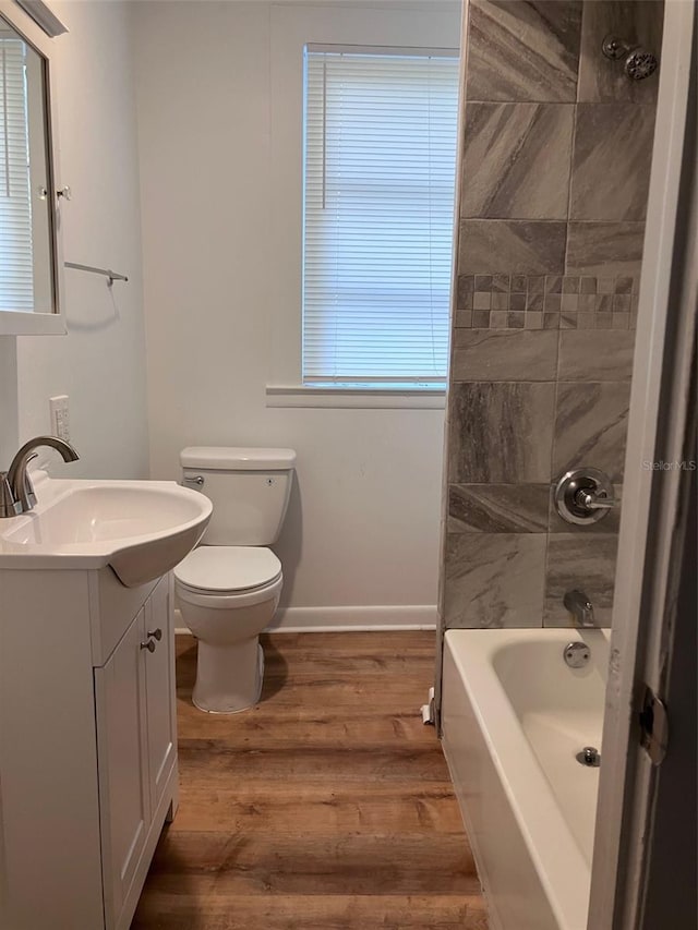 full bath with toilet, baseboards, wood finished floors, washtub / shower combination, and vanity