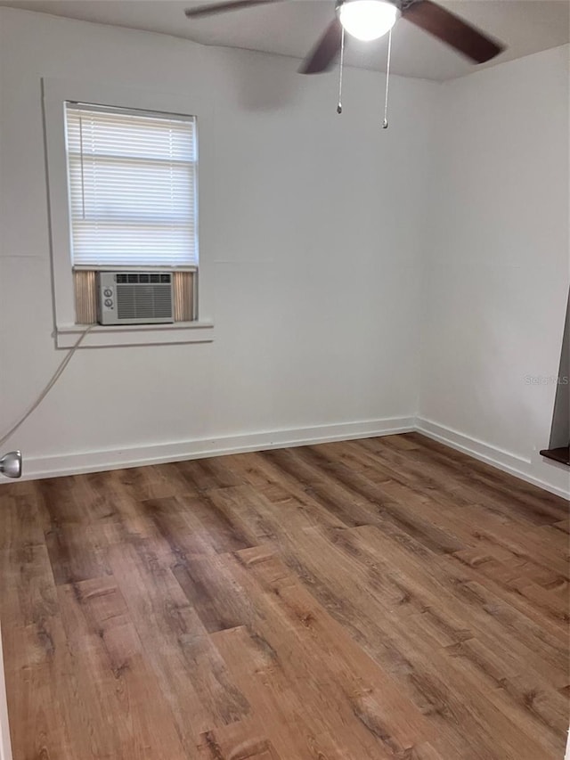 spare room featuring baseboards, wood finished floors, a ceiling fan, and cooling unit