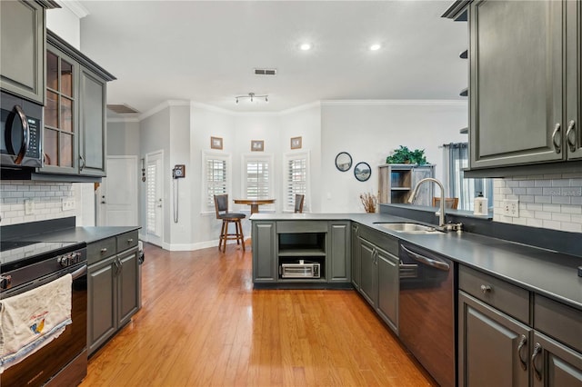 kitchen with light wood-type flooring, a sink, dark countertops, stainless steel appliances, and a peninsula