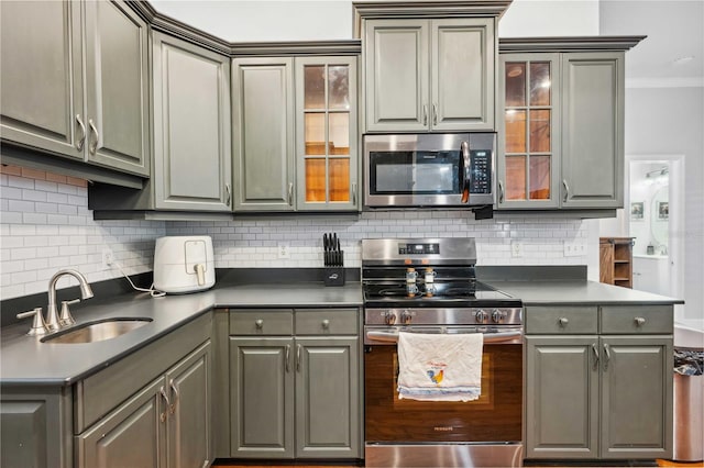 kitchen featuring gray cabinetry, a sink, backsplash, appliances with stainless steel finishes, and crown molding