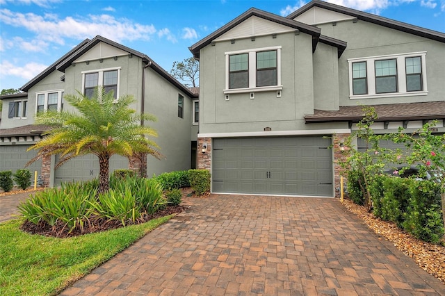 view of front facade featuring stone siding, stucco siding, decorative driveway, and a garage