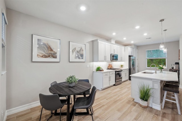 kitchen with a kitchen island with sink, a sink, stainless steel appliances, light countertops, and light wood-style floors