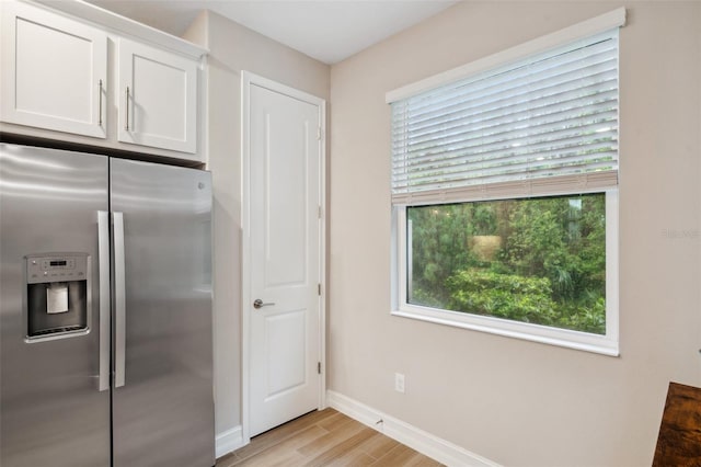 kitchen featuring light wood finished floors, baseboards, stainless steel fridge, and white cabinetry