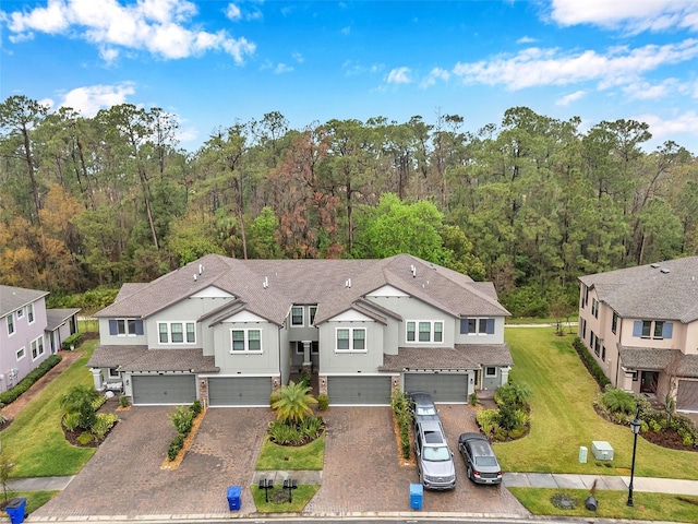 view of front facade featuring a wooded view, decorative driveway, a garage, and a front yard