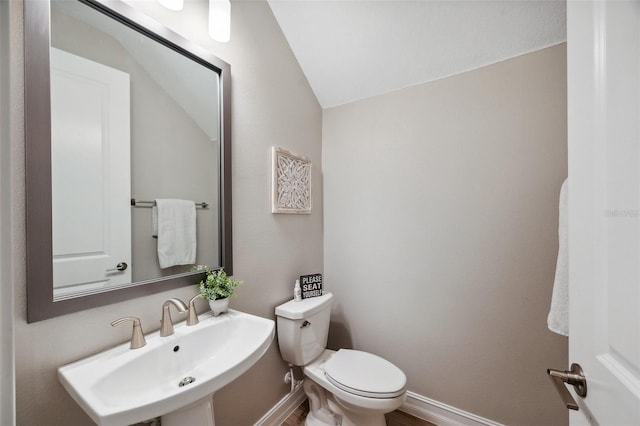 half bathroom with lofted ceiling, toilet, baseboards, and a sink