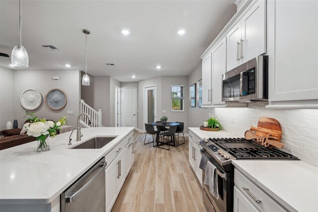 kitchen with backsplash, appliances with stainless steel finishes, light wood-style floors, white cabinetry, and a sink