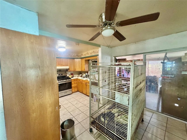 kitchen with stainless steel gas range, light tile patterned flooring, light brown cabinetry, light countertops, and under cabinet range hood