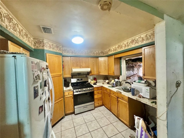 kitchen featuring visible vents, under cabinet range hood, white appliances, light tile patterned flooring, and tile counters