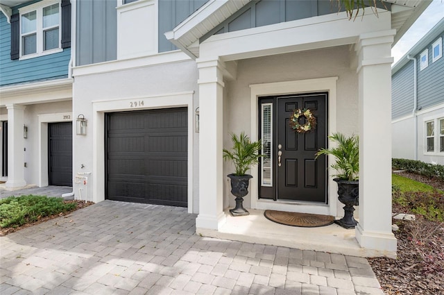 view of exterior entry featuring stucco siding, board and batten siding, decorative driveway, and a garage