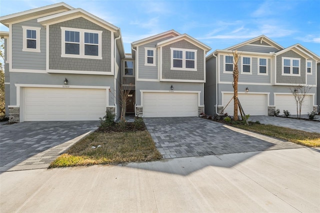 view of front facade featuring stone siding, stucco siding, an attached garage, and decorative driveway