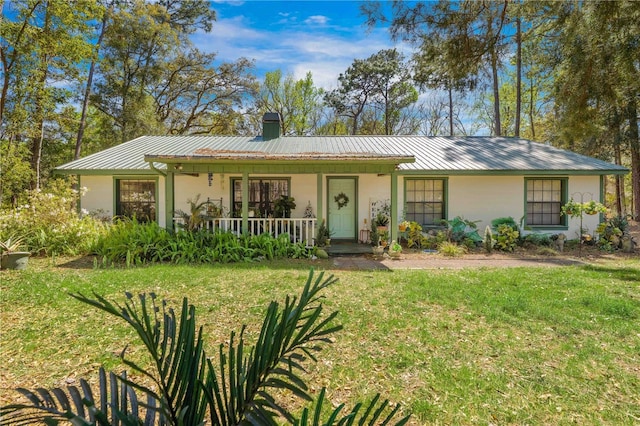 ranch-style house with a front lawn, stucco siding, covered porch, a chimney, and metal roof