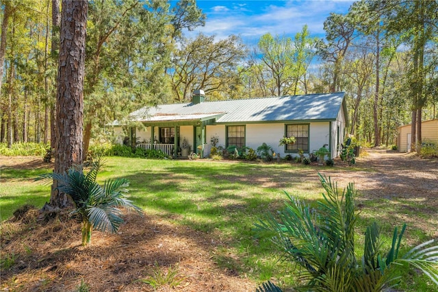 view of front of house with a chimney, covered porch, metal roof, and a front lawn