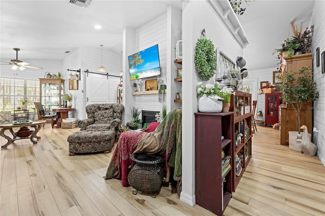 living room with visible vents, a barn door, a fireplace, wood finished floors, and a ceiling fan