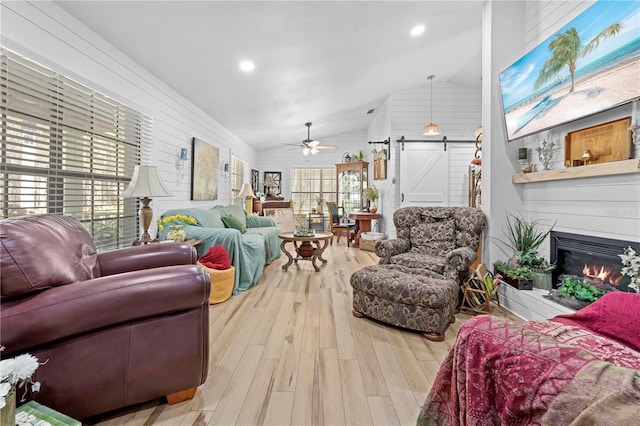 living area with wood finished floors, a ceiling fan, lofted ceiling, a glass covered fireplace, and a barn door