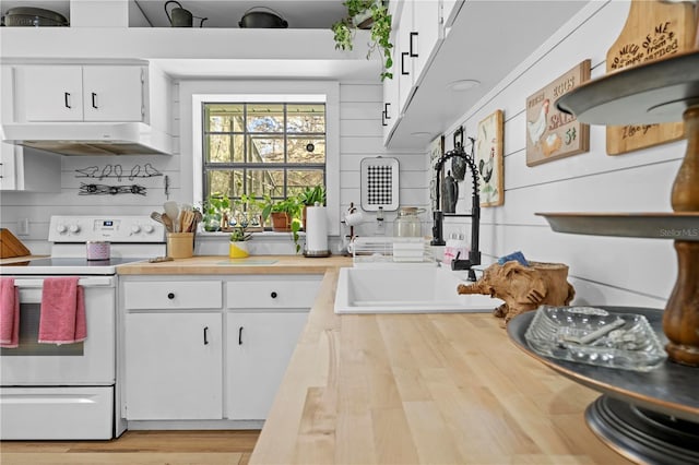 kitchen featuring wooden counters, under cabinet range hood, white cabinets, white electric range, and a sink