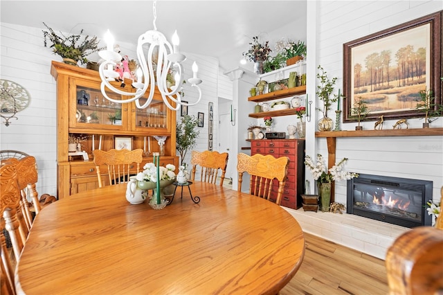 dining area with wood finished floors, a notable chandelier, and a glass covered fireplace