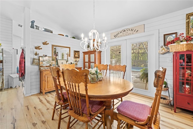 dining space with wooden walls, visible vents, light wood finished floors, and a chandelier