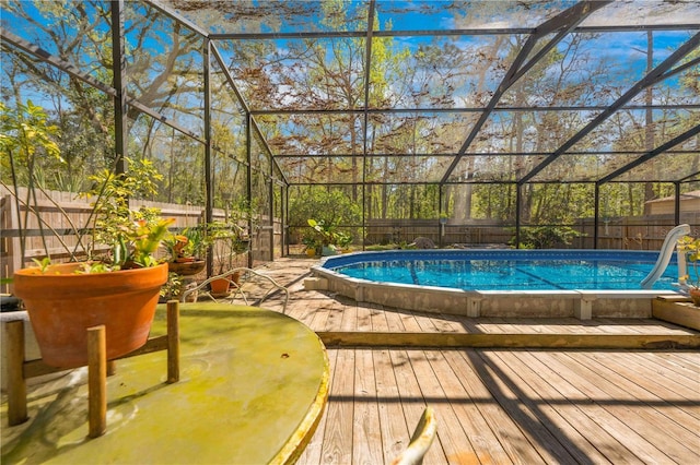 outdoor pool with glass enclosure, a fenced backyard, and a wooden deck