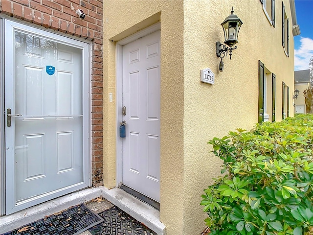 doorway to property featuring brick siding and stucco siding