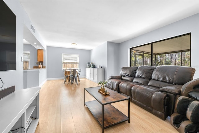 living area with a wealth of natural light, visible vents, baseboards, and light wood finished floors