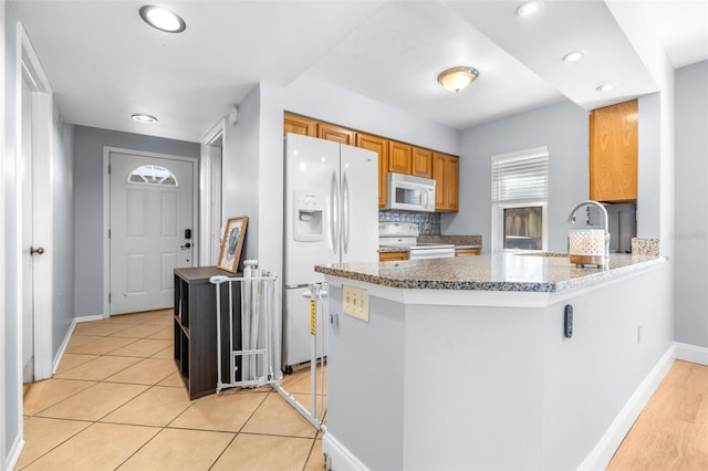 kitchen with white appliances, brown cabinetry, a peninsula, a sink, and decorative backsplash