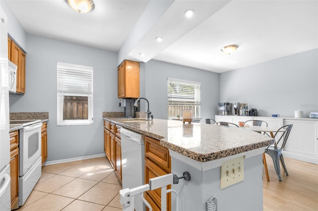 kitchen with a sink, white appliances, a peninsula, and brown cabinetry