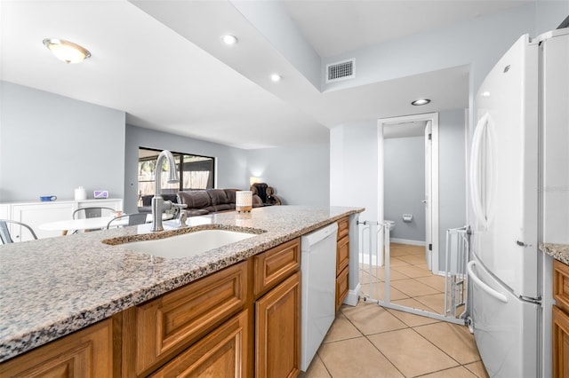 kitchen featuring visible vents, brown cabinets, light tile patterned flooring, white appliances, and a sink