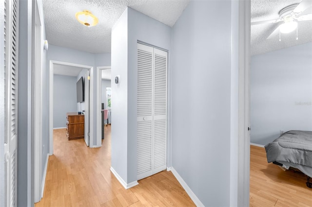 hallway with baseboards, a textured ceiling, and light wood-style flooring